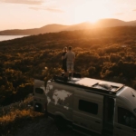 van-camper-wohnbobil-sonnenuntergang-paar-pärchen-berge-aussicht-sonne-orange-urlaub-reisen